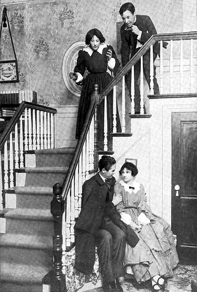 English:   Photograph of a scene from the Broadway production of Little Women Subjects at top of stairs: Marie Pavey (Jo), Donald McLaren (Laurie)
Subjects seated: John Cromwell (John Brooke), Alice Brady (Meg)