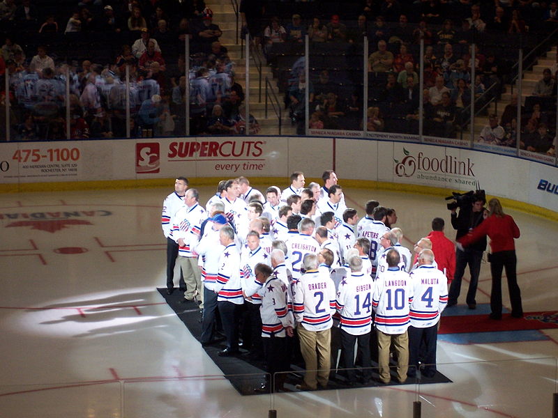 English:   Over 40 former Rochester Americans ice hockey players took advantage of new owner Terry Pegula's offer to fly them in for the 2011 home opener on October 13.  An on-ice ceremony at the Blue Cross Arena preceded the game versus the Scranton/Wilkes-Barre Penguins. Here, the Amerks alumni wait for the entrance of the legendary Joe Crozier, whose induction into the American Hockey League Hall of Fame was announced that evening.
